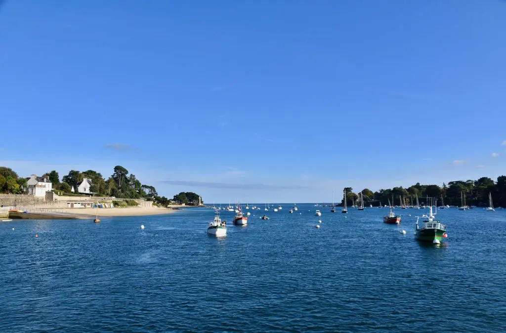 petit port breton avec bateaux amarrés, plage et maisons côtières sous ciel bleu