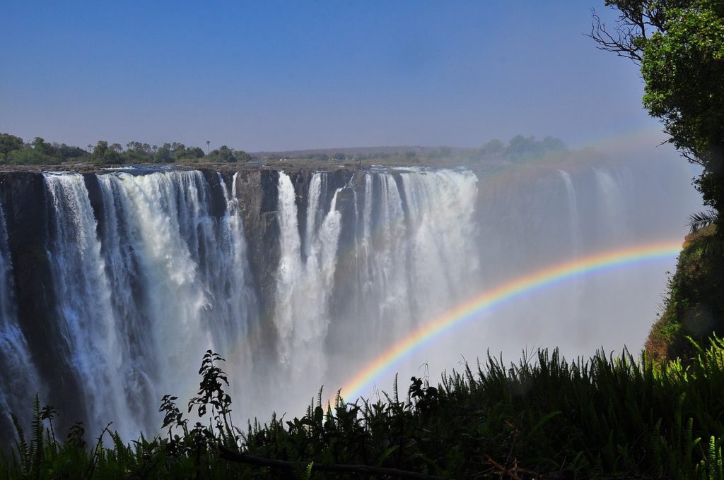 arc-en-ciel sur les chutes Victoria en Zambie avec brume et végétation luxuriante