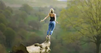 femme sautant sur une bûche dans un paysage montagneux verdoyant, bien-être actif en nature