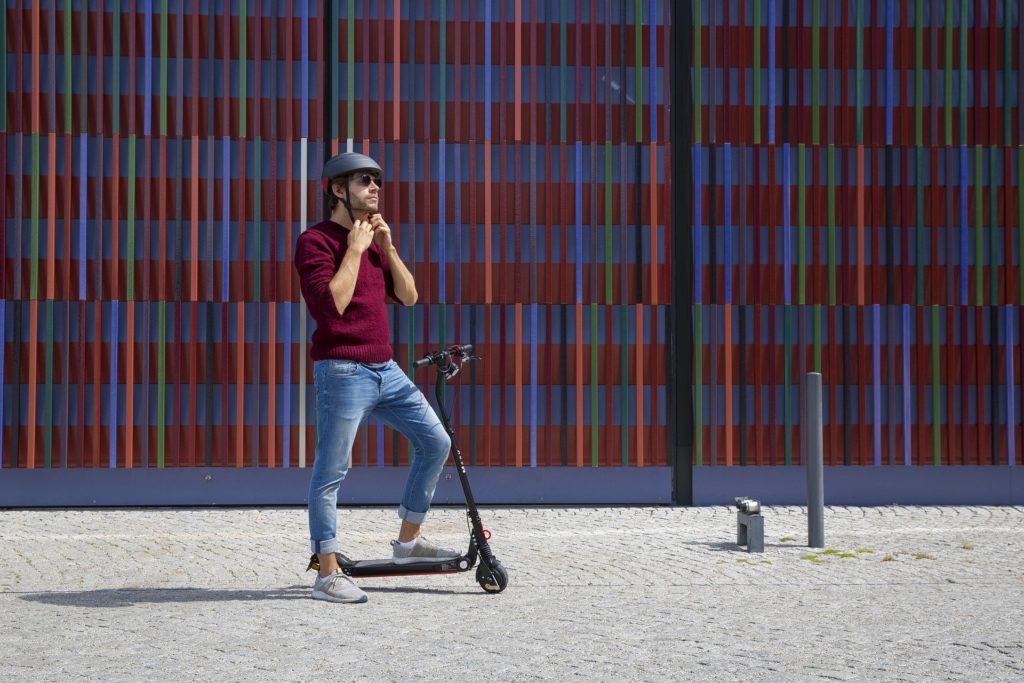 homme en trottinette électrique devant un mur coloré de conteneurs