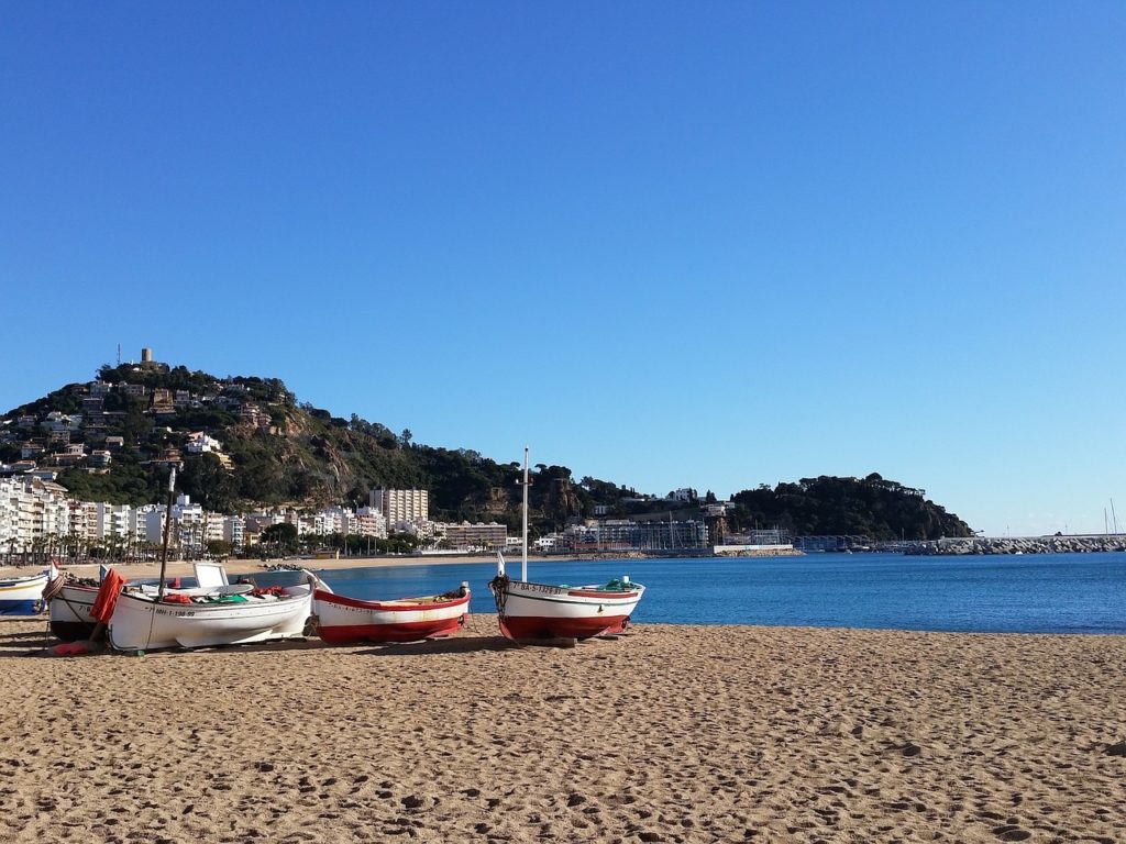 plage méditerranéenne avec barques de pêche colorées et village côtier espagnol sous un ciel bleu