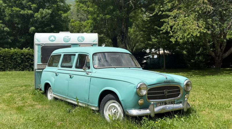 Charming vintage Peugeot and caravan parked in a lush, summer landscape in Saint-Lary-Soulan, France.