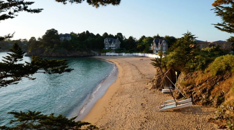 Idyllic beach cove with lush greenery and clear waters in Brittany, France at sunrise.