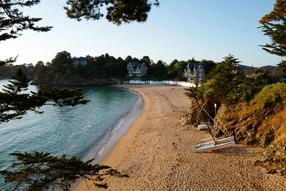 Idyllic beach cove with lush greenery and clear waters in Brittany, France at sunrise.